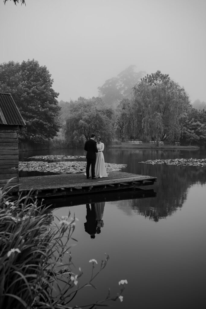Bride and groom standing together on the pier of the Mali Brae Farm lake during candid portrait session